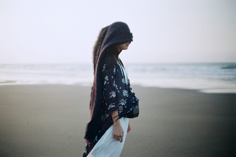 Eine Frau am Strand die eine Decke über den Kopf trägt.