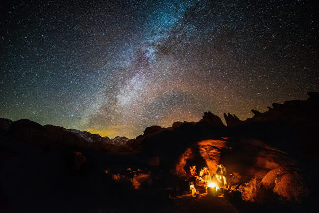 Menschen sitzen um ein Lagerfeuer unter Sternenhimmel