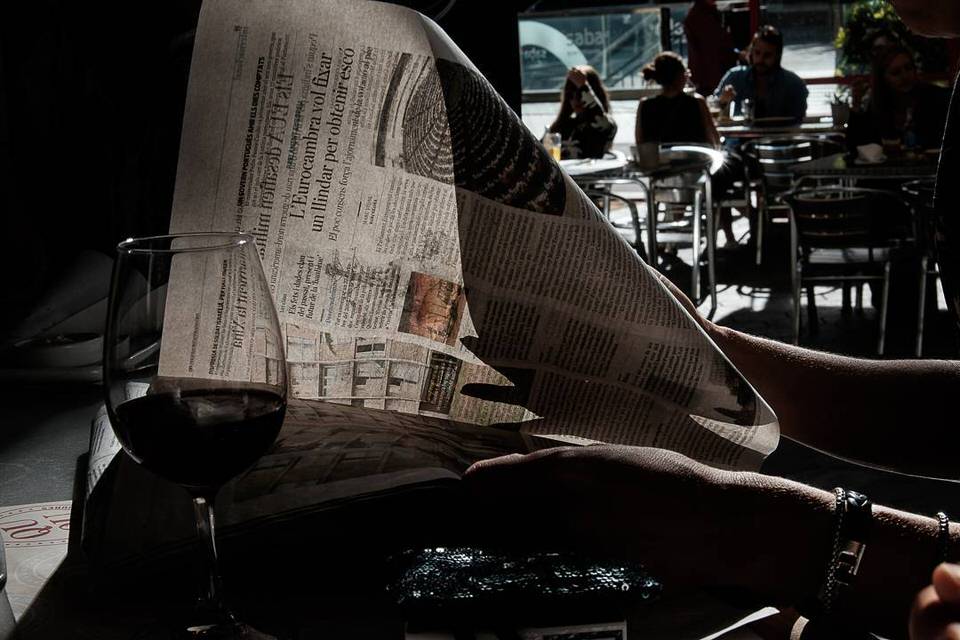 Man sieht ein Glas auf einem Tisch, dahinter eine aufgeschlagene Zeitung durch die man Hindurchblicken kann.