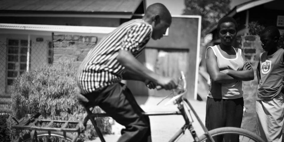 Ein Mann fährt auf einem Fahrrad während eine Frau daneben steht und in die Kamera blickt.