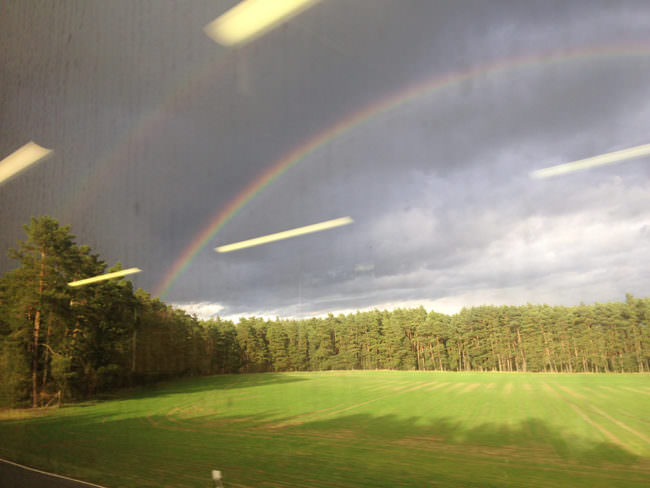 Aufnahme eines Regenbogens in der Landschaft mit Lichtreflexionen auf einer Scheibe.