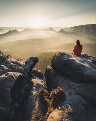 Berglandschaft im Sonnenlicht mit einer Person die auf einem Felsen sitzt.