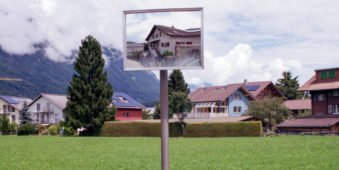 Ansicht einer Ortschaft mit einem Sichtspiegel der verzerrt ein Haus abbildet.