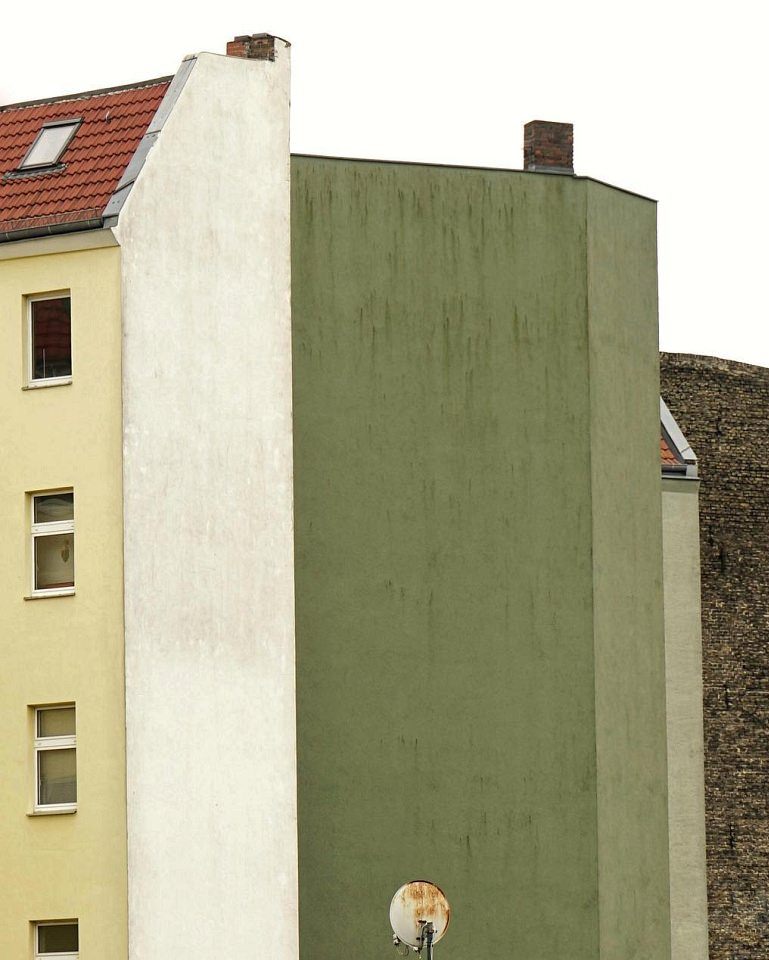 Hausfassaden in Gelb, Grün und Braun, davor eine Satellitenschüssel.
