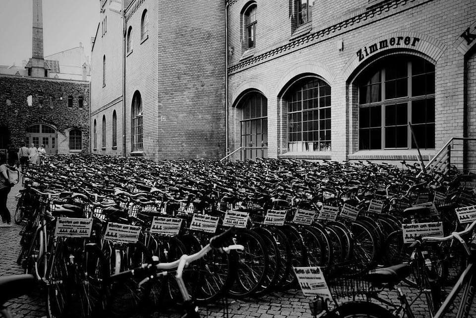 Schwarzweiße Aufnahme von ganz vielen Fahrrädern vor einer Industriekulisse.