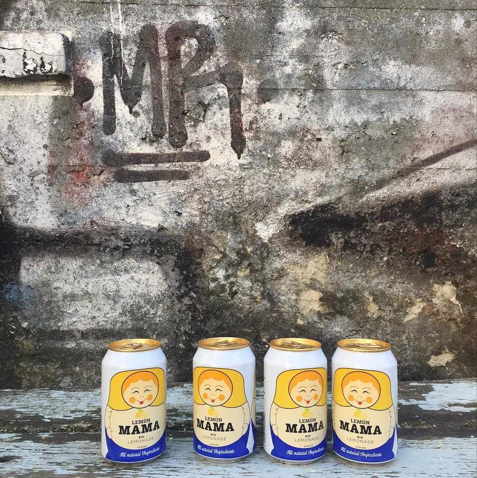Vier Getränkedosen mit Matroskaaufdruck vor einer rustikalen Betonwand mit Graffito.