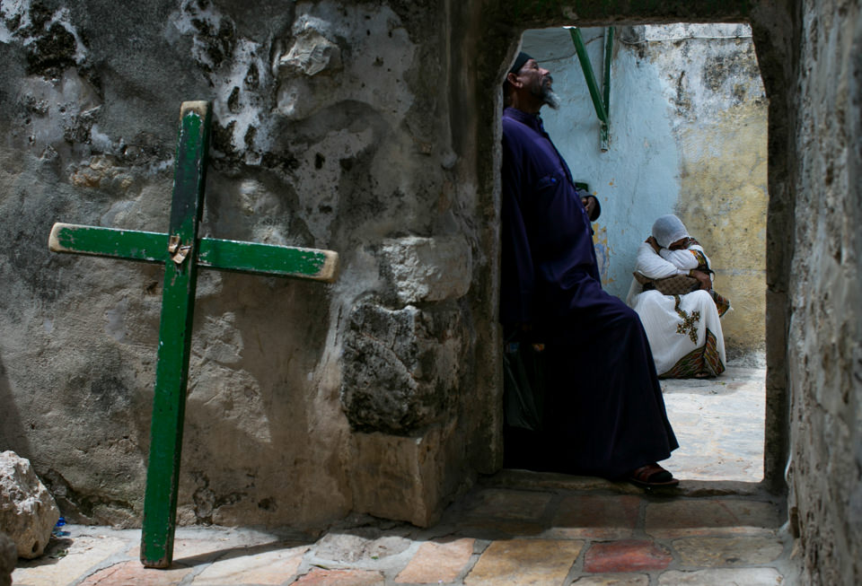 Ein Kreuz steht neben einer Tür, dahinter beten Menschen