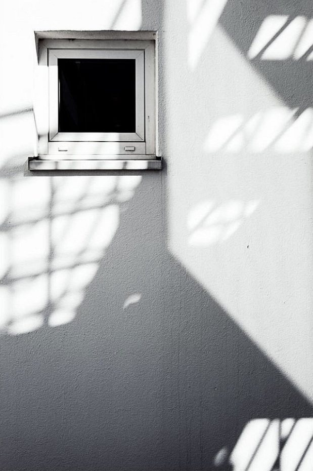 Licht- und Schattenspiel auf einer weißen Fassade mit kleinem Fenster.