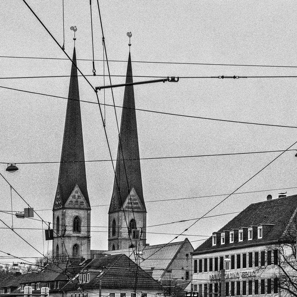 Oberleitungen vor den Dächern einer Stadt mit Kirche.