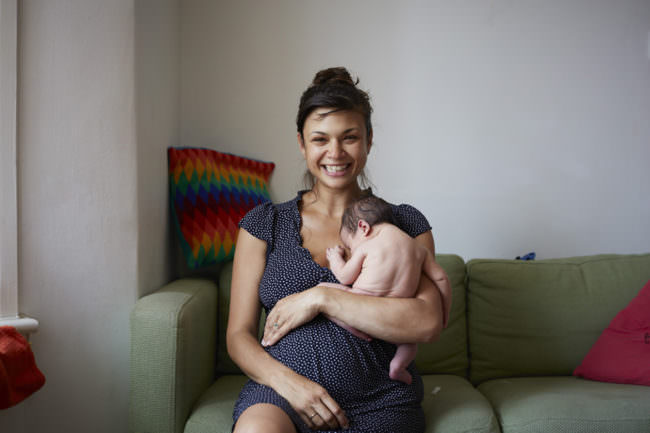Junge Frau lachend mit nacktem Säugling im Arm.