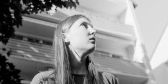 Schwarz-weiß Fotografie einer jungen Frau vor einer Hausfassade