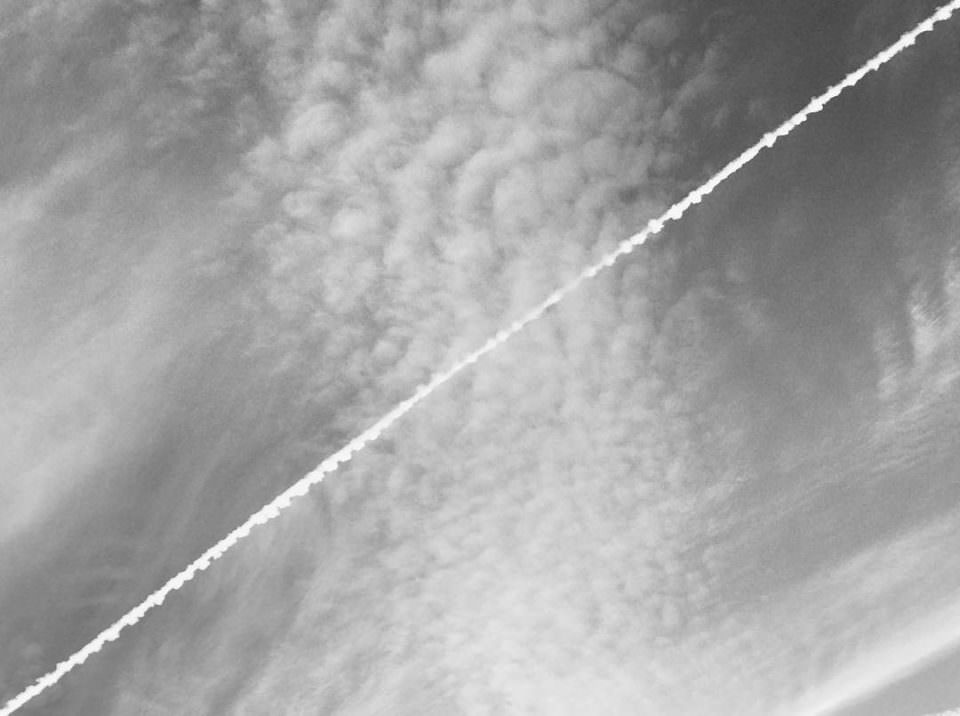 Ein Himmelbild mit Schäfchenwolken, dass von einer Fluglinie diagonal gekreuzt wird.