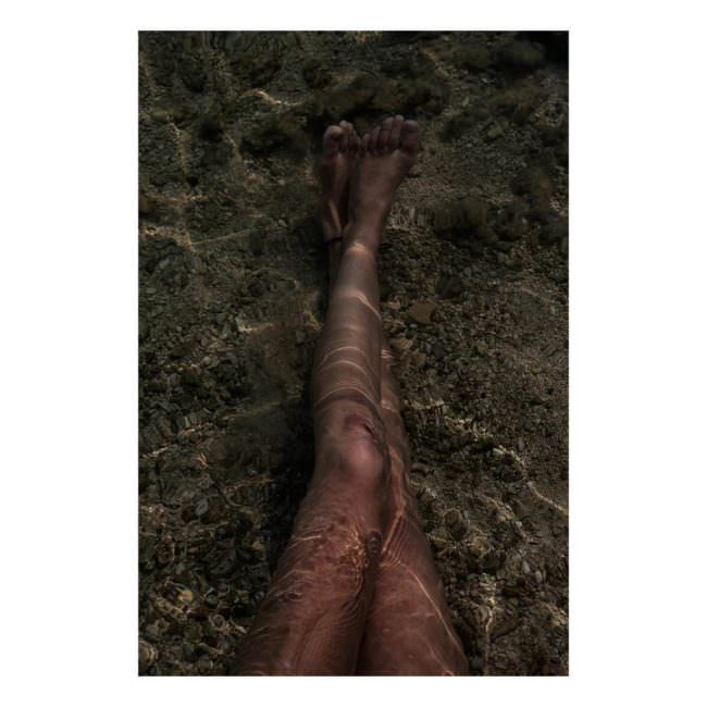 Zwei übereinandergeschlagene Beine unter Wasser auf sandigem Boden.