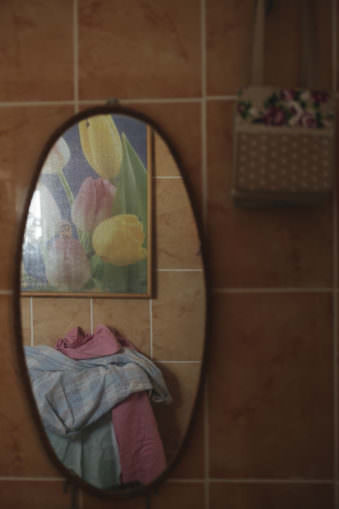 Ansicht eines ovalen Wandspiegels, in dem sich Stoffe und ein Tulpenbild spiegeln.