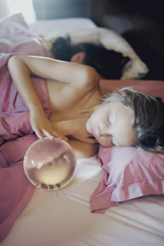 Kind liegt in einem Bett unter rosa Bettwäsche und schaut in eine Glaskugel.