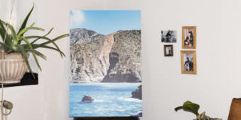 Bild einer Küstenlandschaft mit Türkisen Meer steht in einer Zimmerecke, daneben kleinen gerahmte Fotografien an einer Wand.