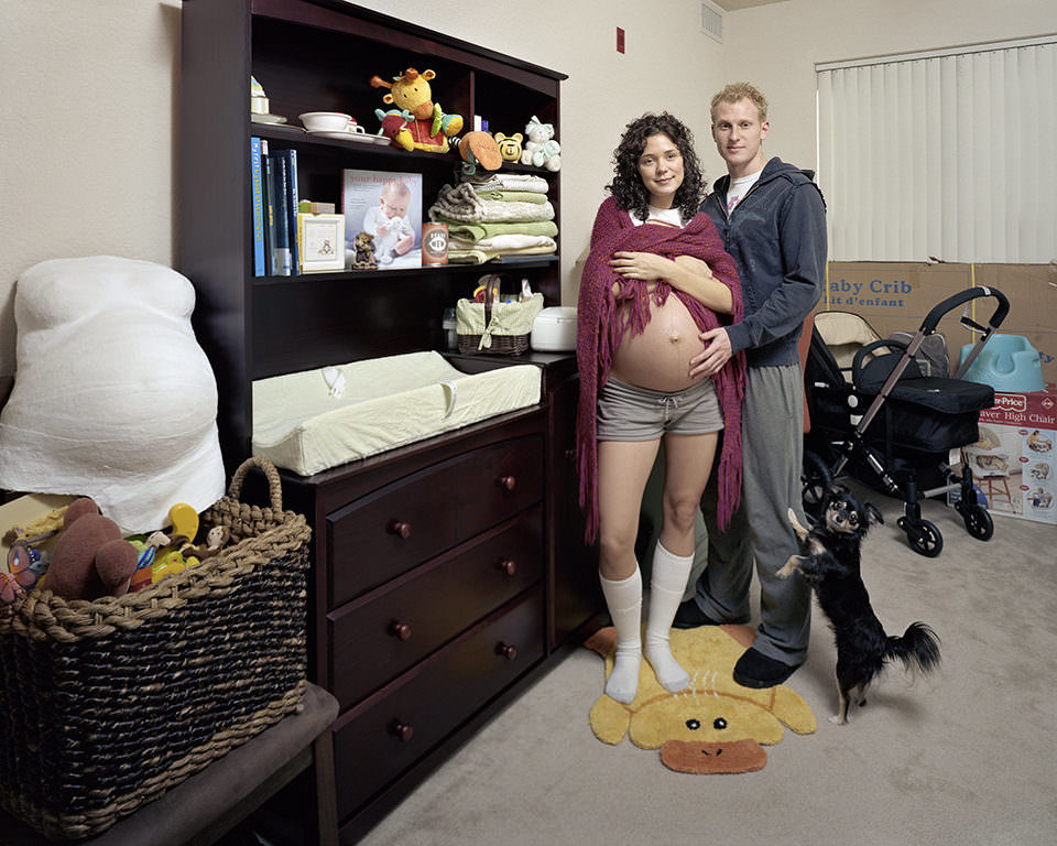 Eine schwangere Frau mit nacktem Bauch und ein junger Mann stehen in einem Raum mit Ententeppich.