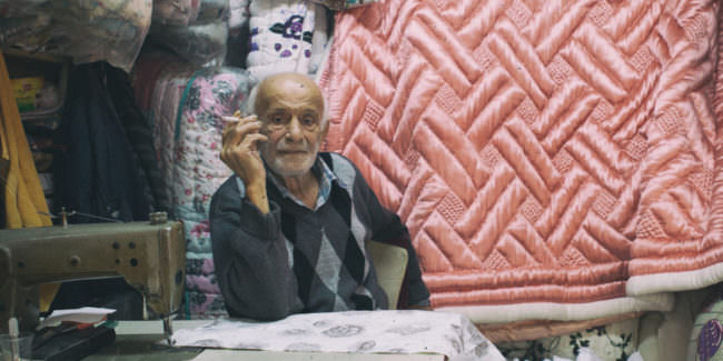 Rauchender Mann sitzt hinter einer Nähmaschine in einem kleinen Laden für Bettdecken.