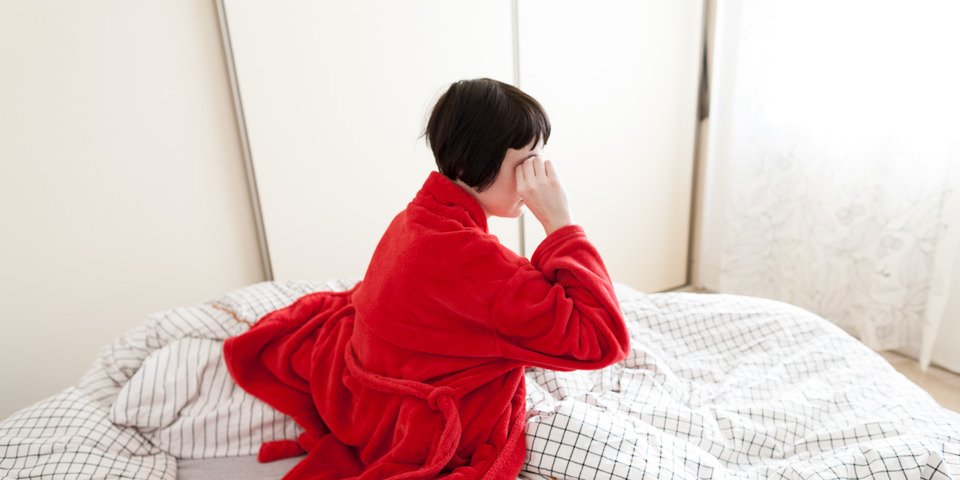 Frau im roten Bademantel sitzt in ihrem Bett