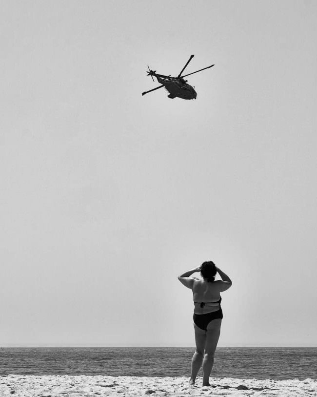Frau sieht am Strand zu einem Hubschrauber