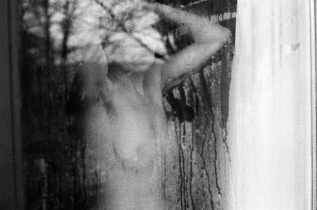 Nackte Frau durch ein verregnetes Fenster