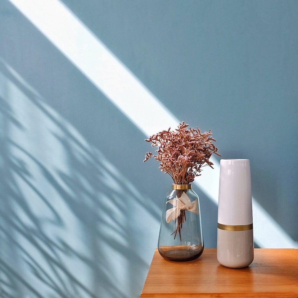 zwei Vasen und ein Blumenstrauß auf einem Tisch vor blauer Wand mit Lichtstreifen und Schatten