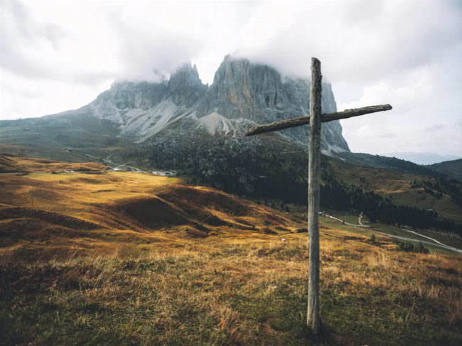 Ein Holzkreuz im Vordergrund, im Hintergrund Berge