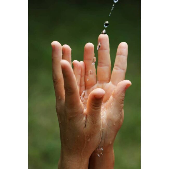 Zwei Hände greifen nach einem Strahl Wasser