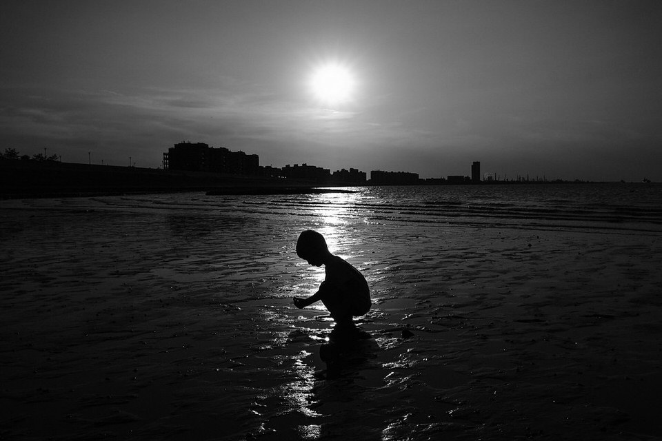 Ein Kind im Schattenriss kniet im Watt