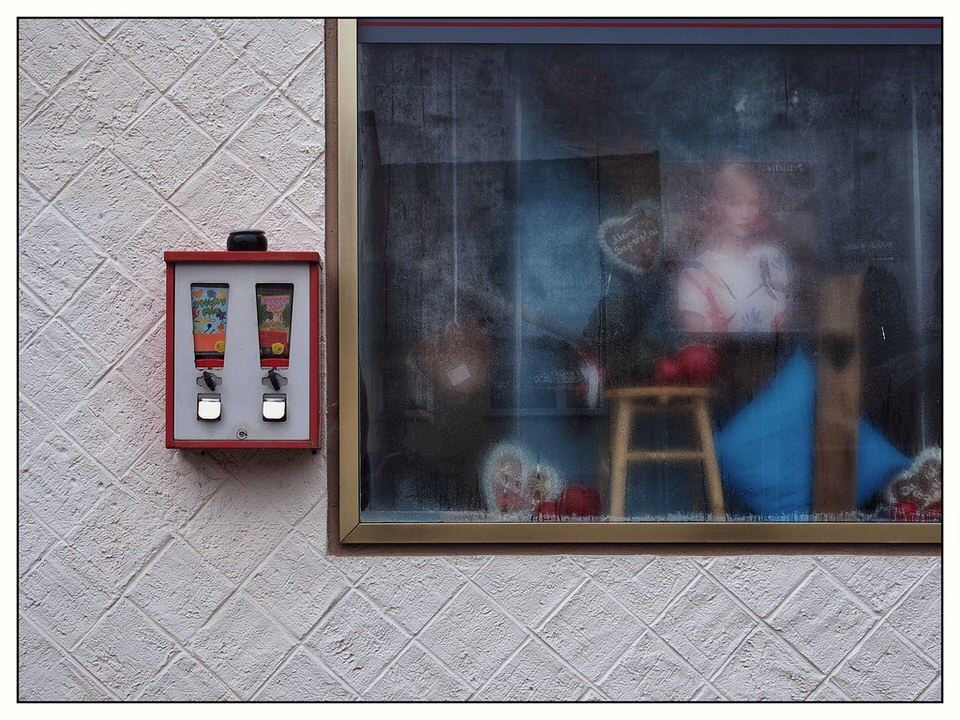 Ein Schaufenster und daneben ein Kaugummiautomat auf dem ein Aschenbecher steht