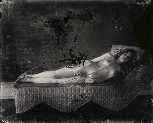 Eine nackte Frau liegt in starrer Pose auf einem Canapé