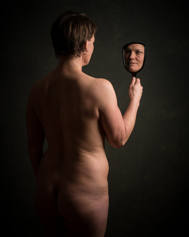 Eine nackte Person sieht sich durch einen Spiegel an