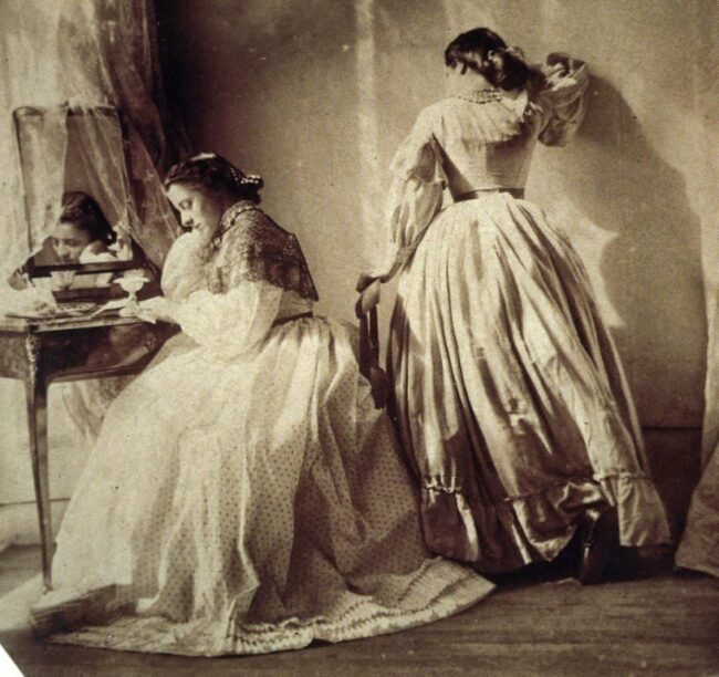 zwei Frauen, eine sitzt am Schreibtisch, die andere lehnt an der Wand