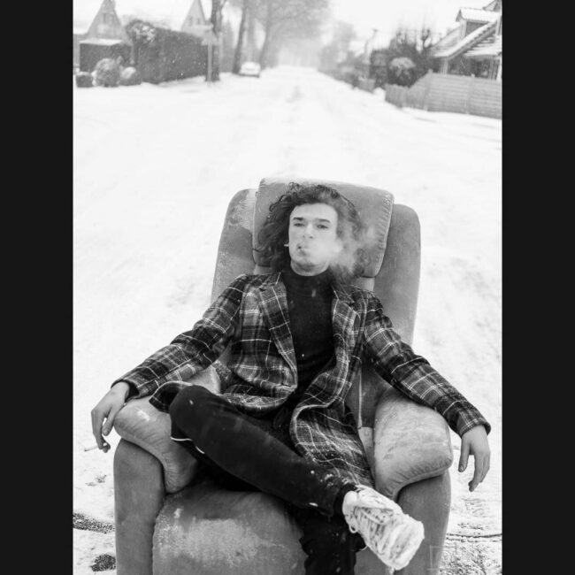 Mann sitzt rauchend in einem Sessel im Schnee
