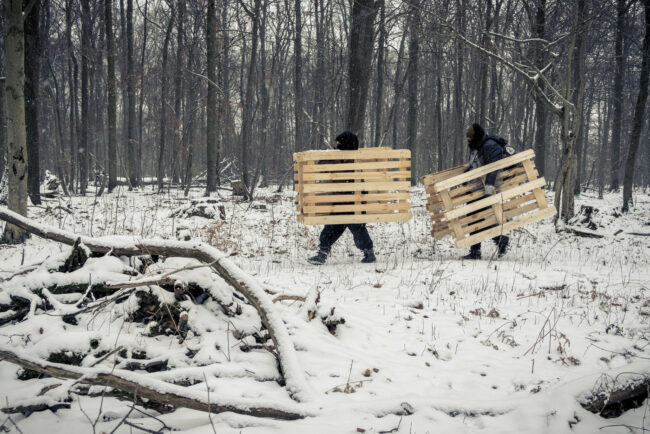 Zwei Menschen tragen im Schnee Paletten durch den Wald