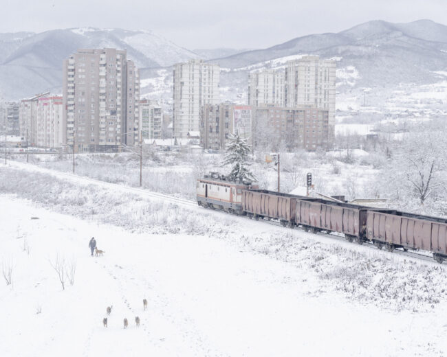 Zug fährt im Winter neben einer Plattenbausiedlung