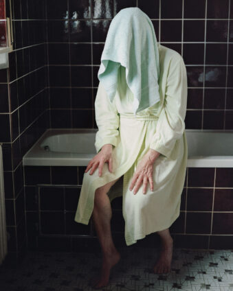 Person an iner Badewanne mit Handtuch vor dem Gesicht