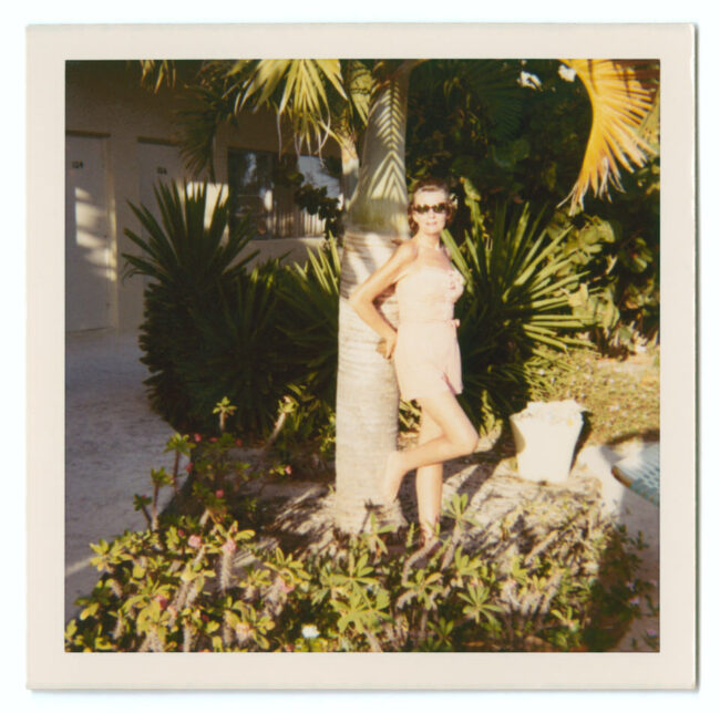 Polaroid einer Frau, die an einer Palme lehnt