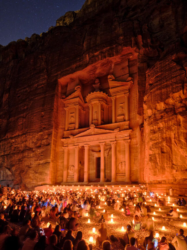 Temoel in rotem Felsen bei Nacht. Davor Menschen mit Lichtern