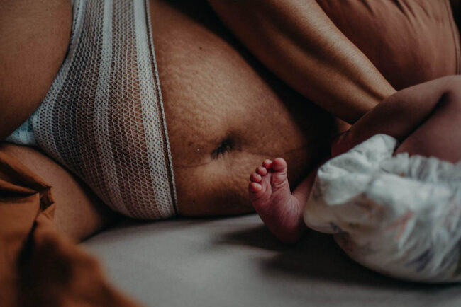 Detailansicht von Babybeinen und dem Unterleib einer Person mit Netzunterwäsche