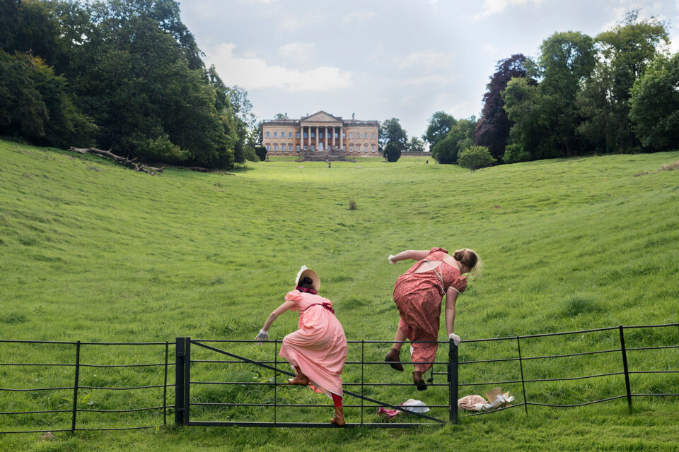 Zwei Personen in Kleidern springen über einen Zaun