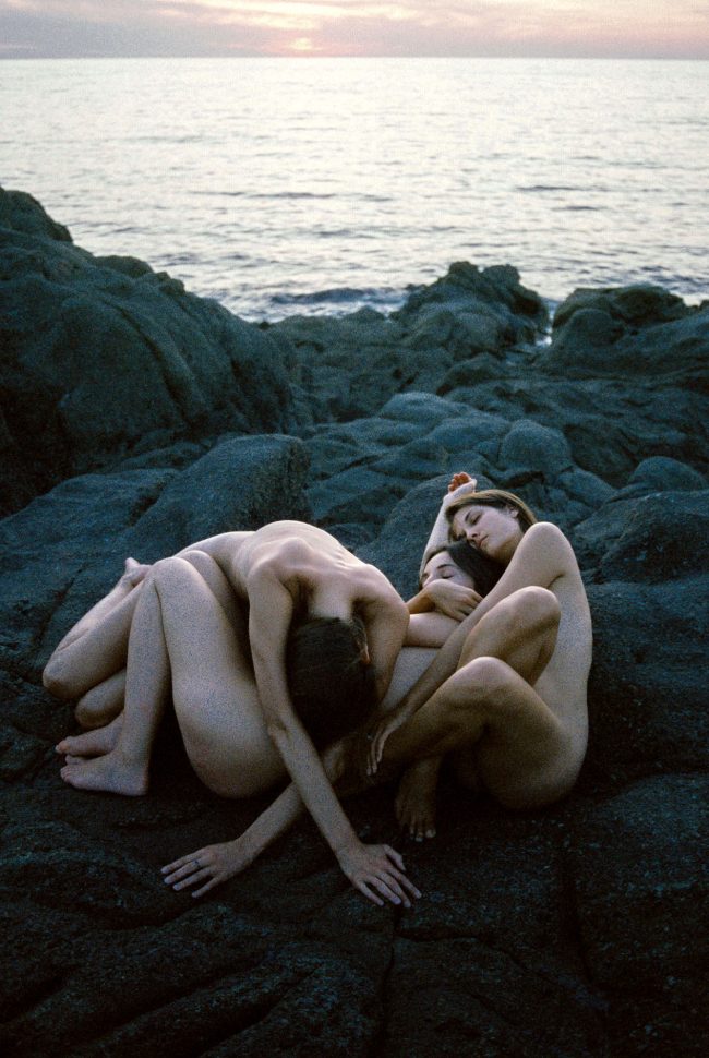 Menschen nackt an einem Steinstrand liegen übereinander