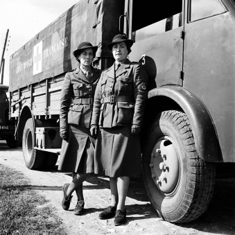 Zwei Frauen in Uniformen vor Rot-Kreuz-Lastern.