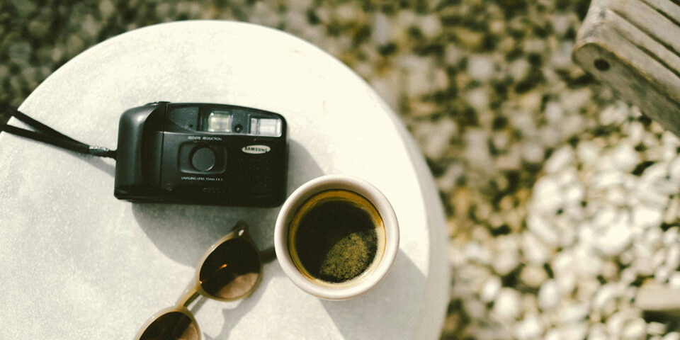 Kamera, Kaffee und Sonnenbrille auf einem Tisch